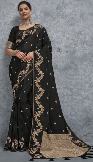 Black silk saree with intricate gold zari embroidery, featuring floral vine motifs and a richly woven traditional border, elegantly draped on a model against a grey textured background – perfect for wedding and festive wear.