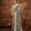 Woman wearing elegant off-white silk saree with black floral print and rich golden zari woven border, paired with matching blouse and traditional jewelry in a heritage-inspired setting.