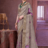 Elegant woman wearing a grey silk saree with golden zari border and purple floral prints, styled with traditional jewelry, standing in a royal vintage indoor setting.
